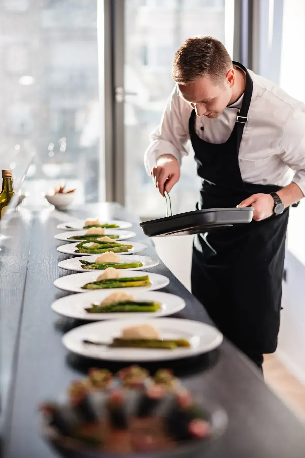 A chef finishing a row of plated asparagus courses along a service pass